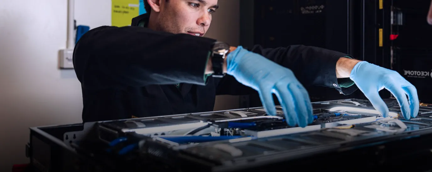 Technician wearing blue gloves working on server hardware inside a data center rack.