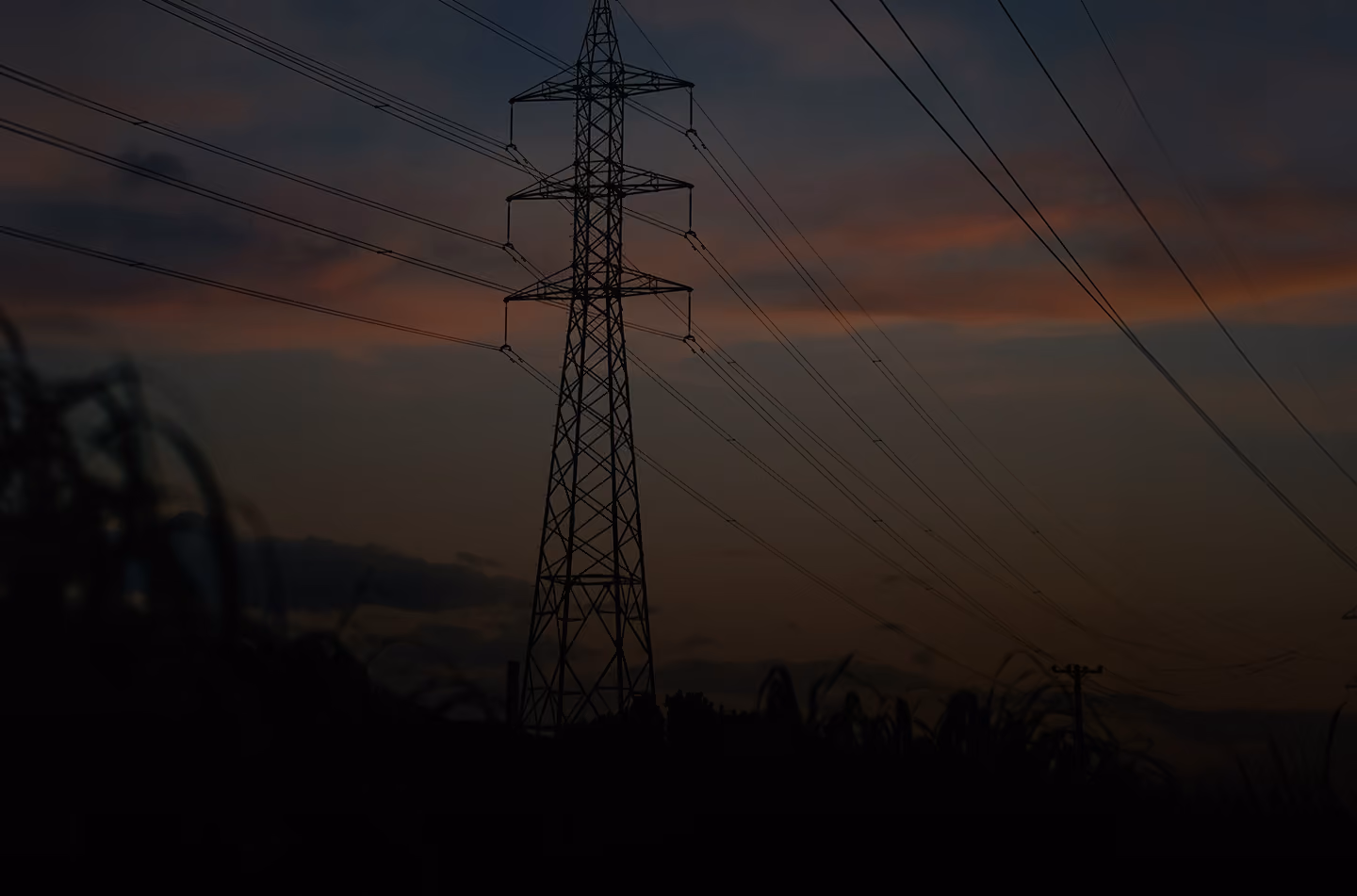 Silhouette of an electrical transmission tower and power lines against a sunset sky.