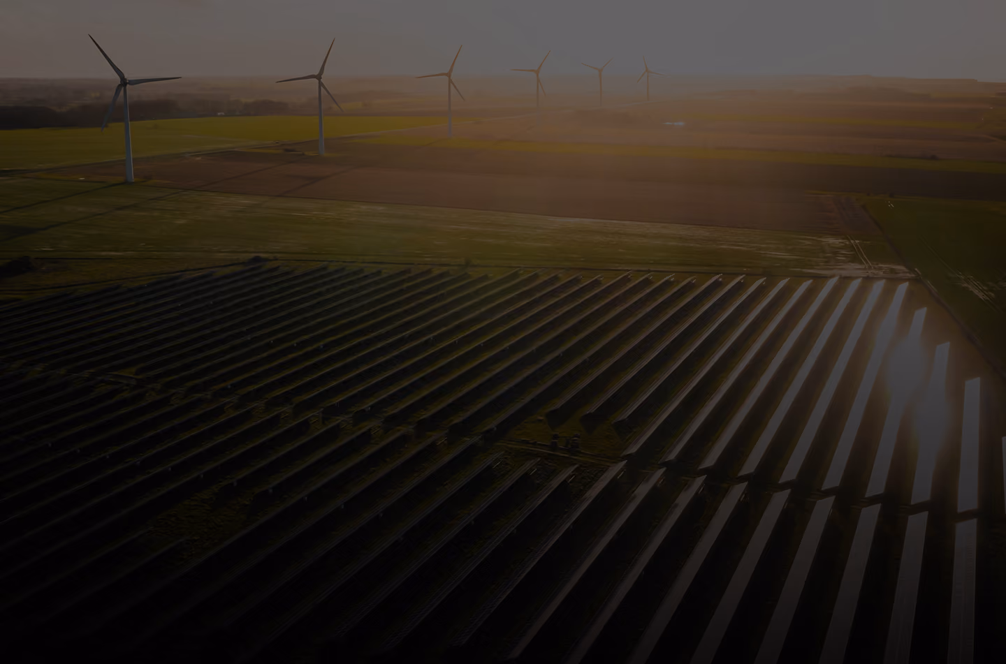 Aerial view of solar panels and wind turbines on green farmland at sunset.