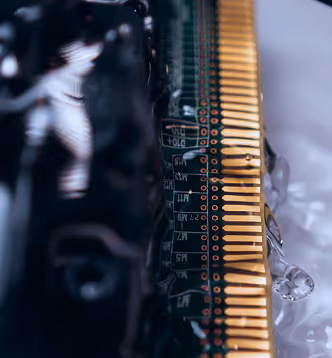 Close-up of a circuit board’s golden connector pins with water droplets on its surface.
