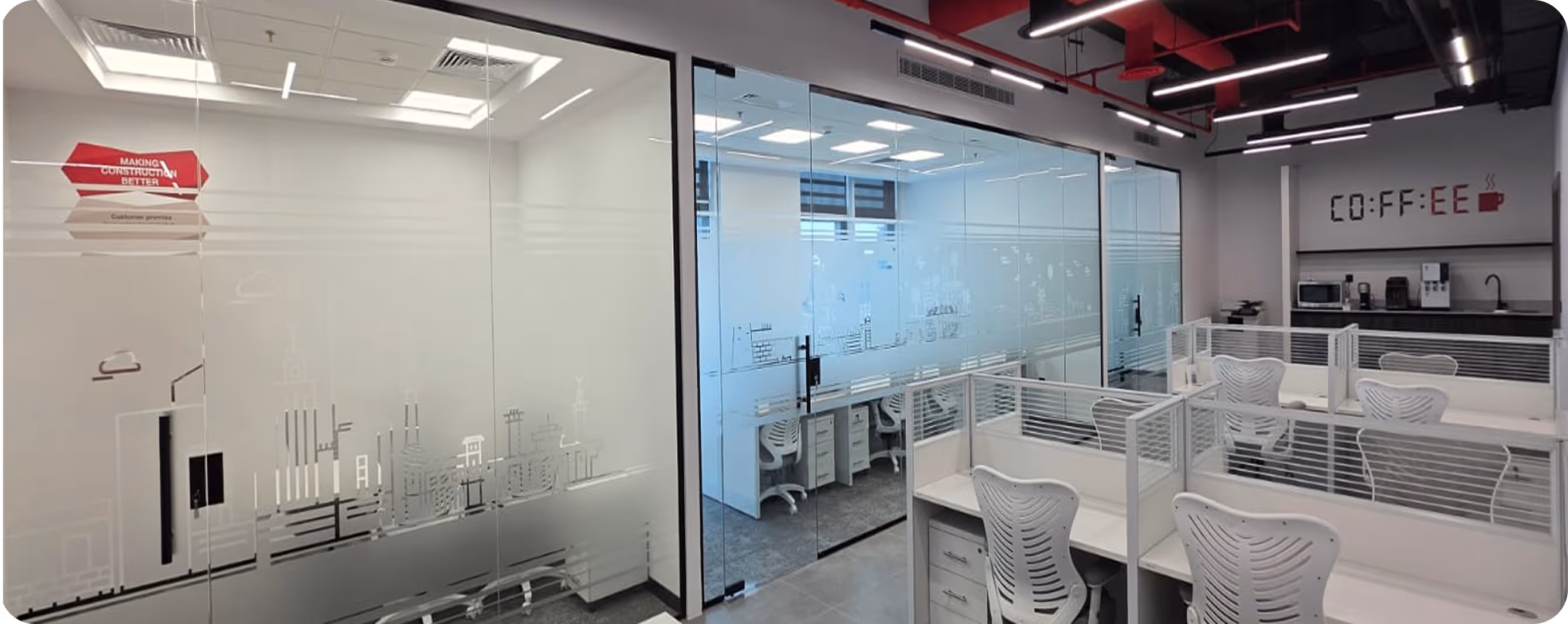 Modern office space with glass-walled conference rooms, multiple white cubicles with ergonomic chairs, and a coffee station against the wall.