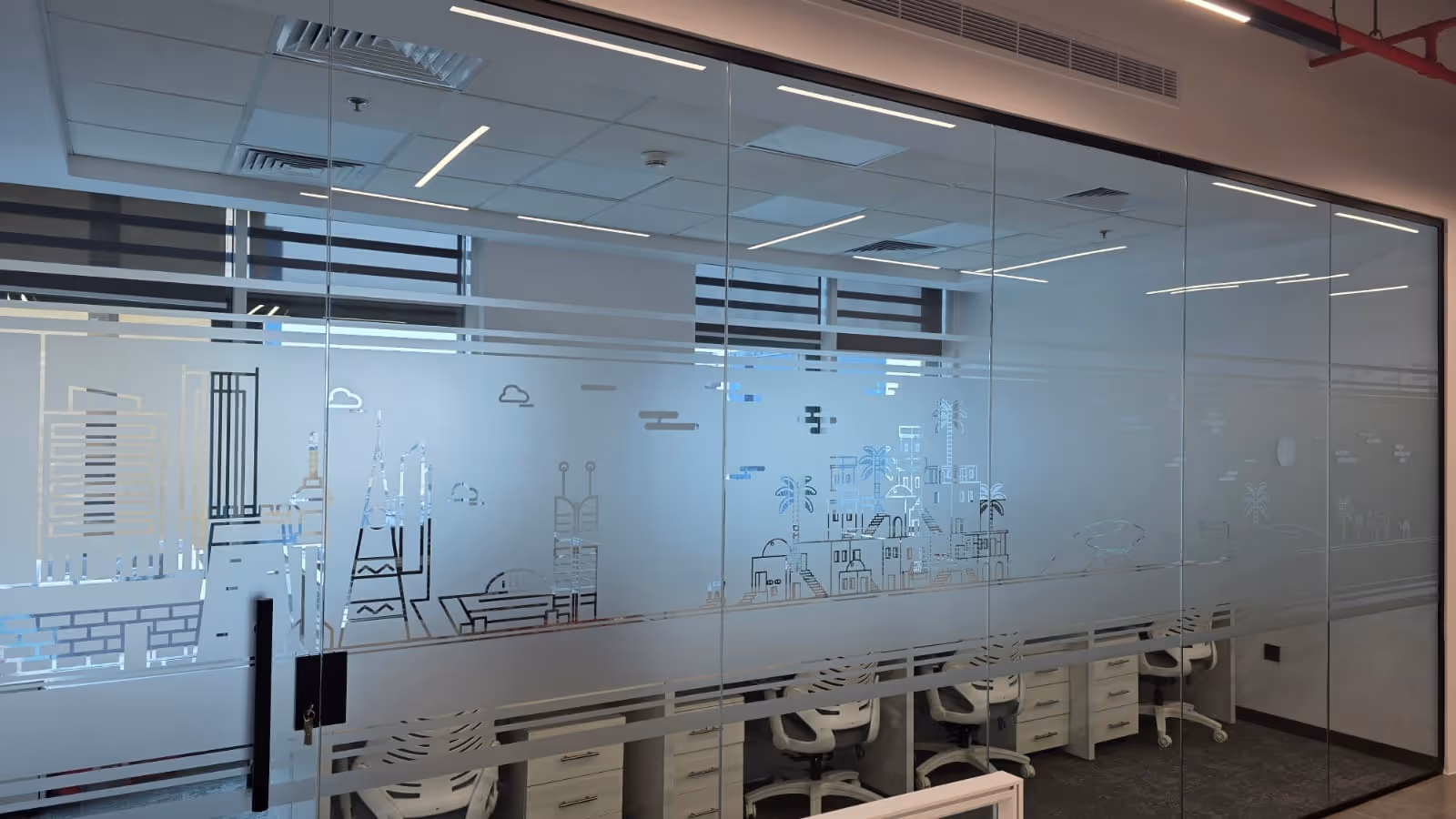 Modern office meeting room with glass walls featuring etched cityscape and palm tree designs.