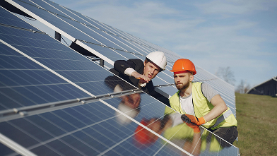 Two workers in safety helmets inspecting solar panels in an outdoor solar farm.