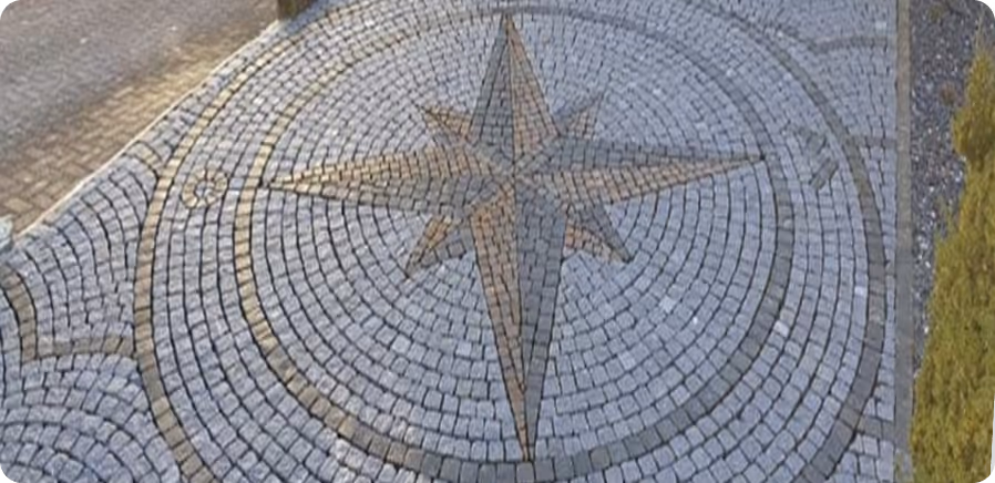 Großes Pflastermosaik auf einem Gehweg mit einem Kompassrosenmotiv aus Steinquadern.