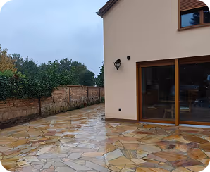 Hausecke mit großen Fenstern und nassem, steinernem Boden nach Regen bei bewölktem Himmel.