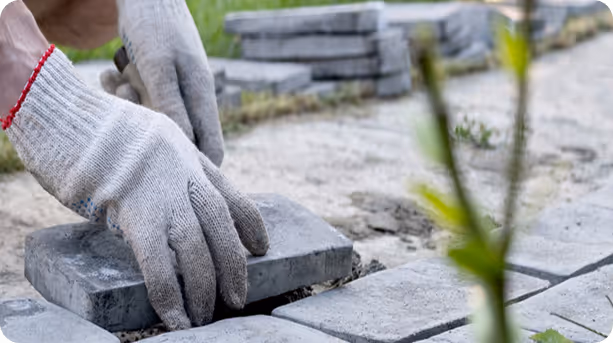 Hände mit Arbeitshandschuhen legen graue Pflastersteine für einen Gehweg.