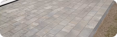 Graue Pflastersteine auf einem Bürgersteig neben einem Beet mit Erde.