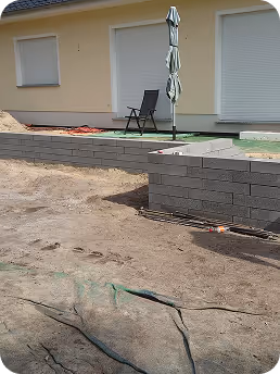 Haus mit Terrasse in Bauphase, mit aufgestellt geschlossenem Sonnenschirm und Stuhl vor zwei geschlossenen Fenstern.