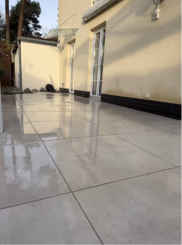 Nasse, glänzende Steinplatten auf einer Terrasse vor einem hellen Haus mit einer großen Glasschiebetür.