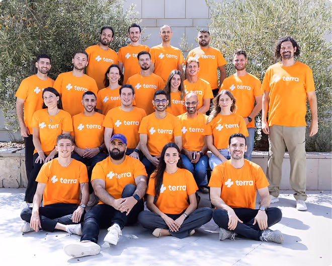 Group of 23 people wearing matching orange Terra t-shirts posing outdoors, some standing and some sitting.