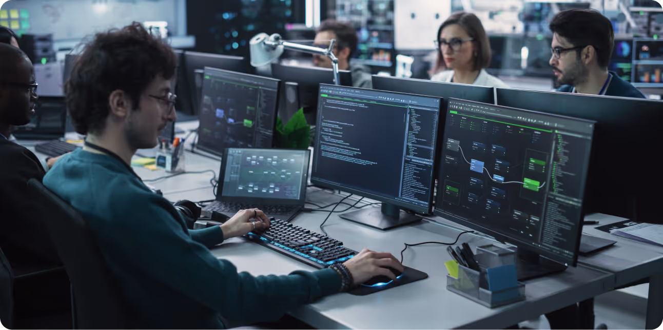 Software developers working at desks with multiple monitors displaying code and workflow diagrams.