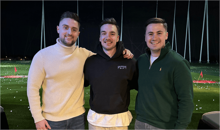 Drei Teammitglieder in Freizeitkleidung auf einer Driving Range bei Nacht, lockere Teamstimmung.