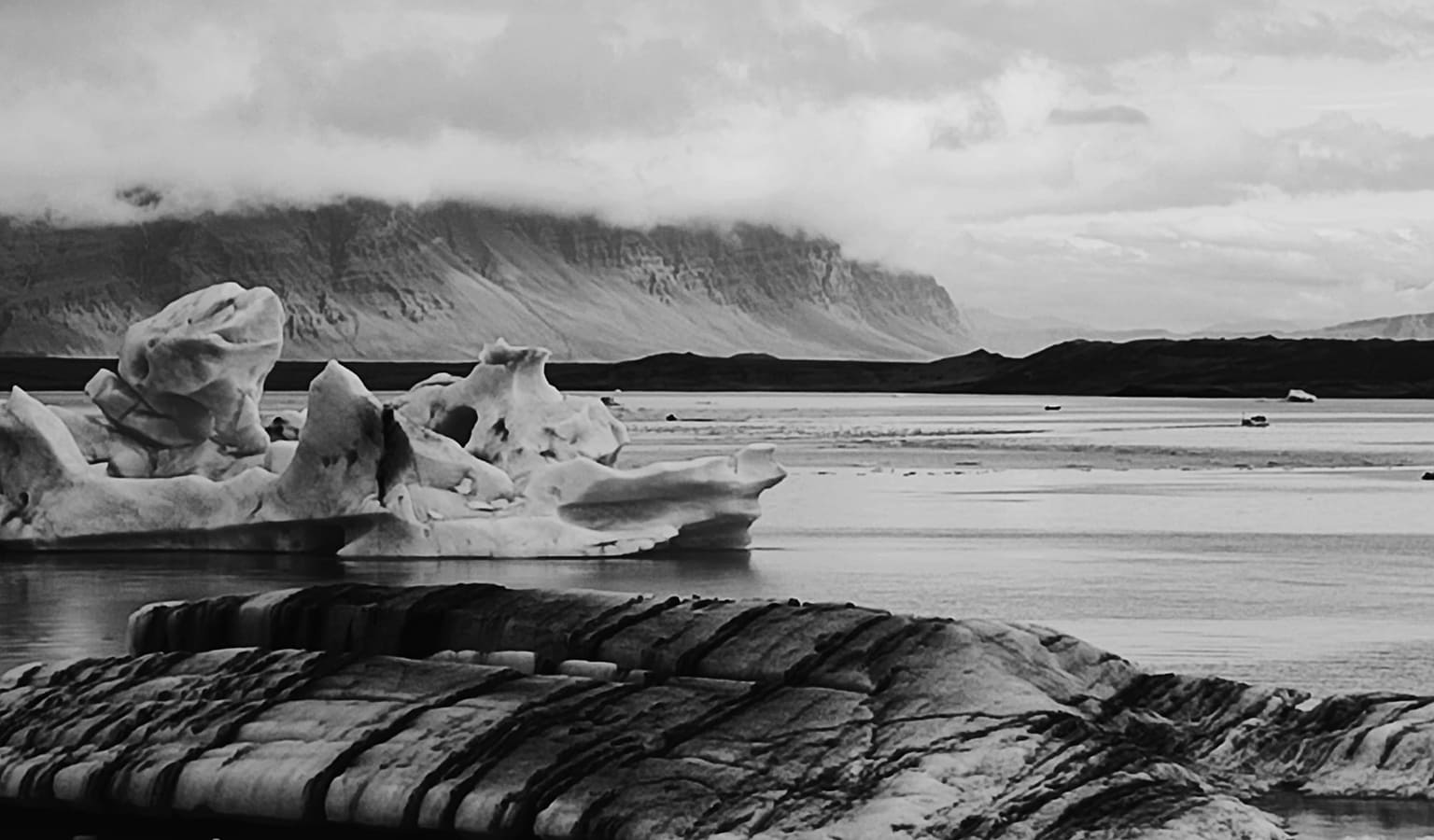 Black and white photograph of ice formations on a glacial lagoon in Iceland, a flat-topped mountain behind under heavy cloud.