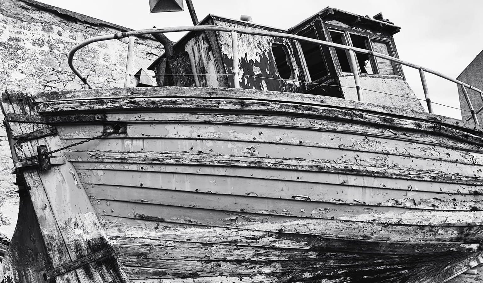Black and white photograph of an old wooden fishing boat with peeling paint, propped up out of the water.