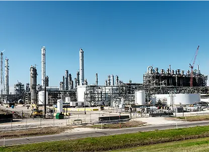 Large industrial refinery facility with storage tanks, pipes, and distillation towers under a clear blue sky.