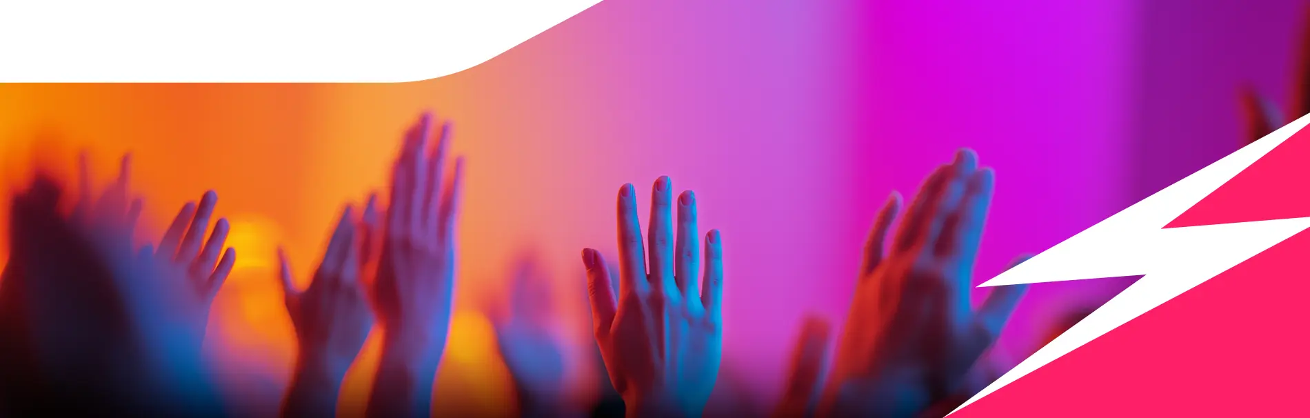 Raised hands in a crowd illuminated by colorful orange, pink, and blue lighting.