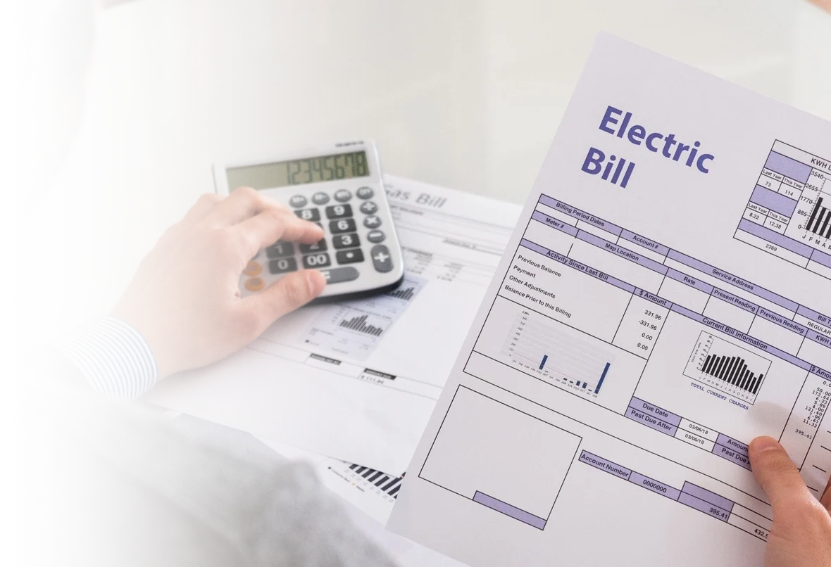 Person using a calculator while holding an electric bill with charts and payment details.