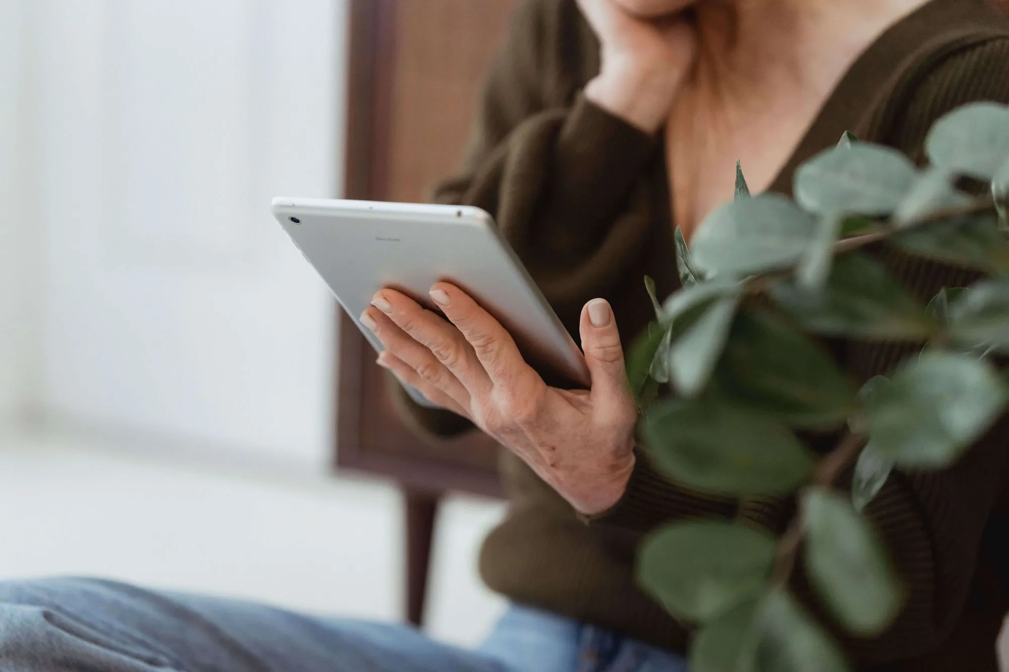 An older person holding a tablet beside a houseplant