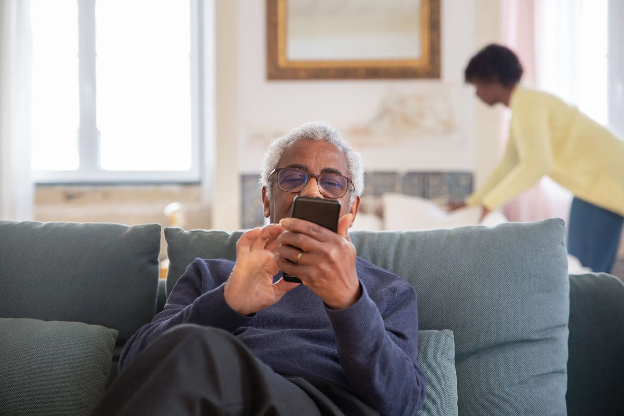 An older man reading an update on his phone on the sofa at home