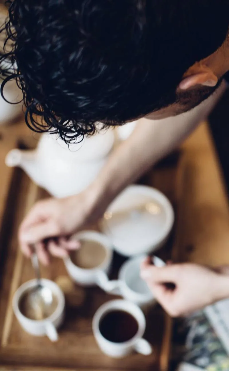 Two people sharing a pot of tea at a wooden table, seen from above