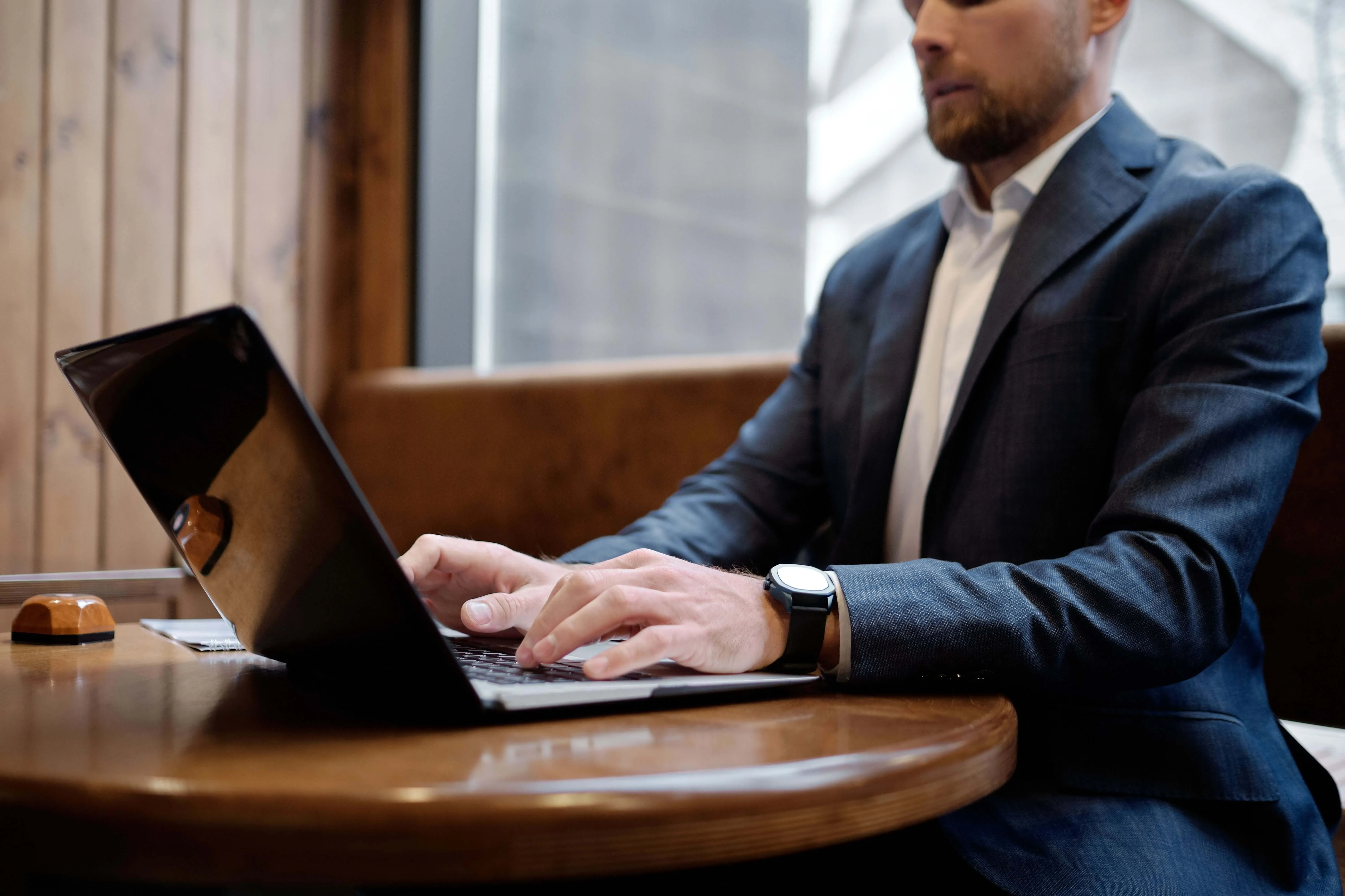 A man in a suit working on a laptop at a wooden table