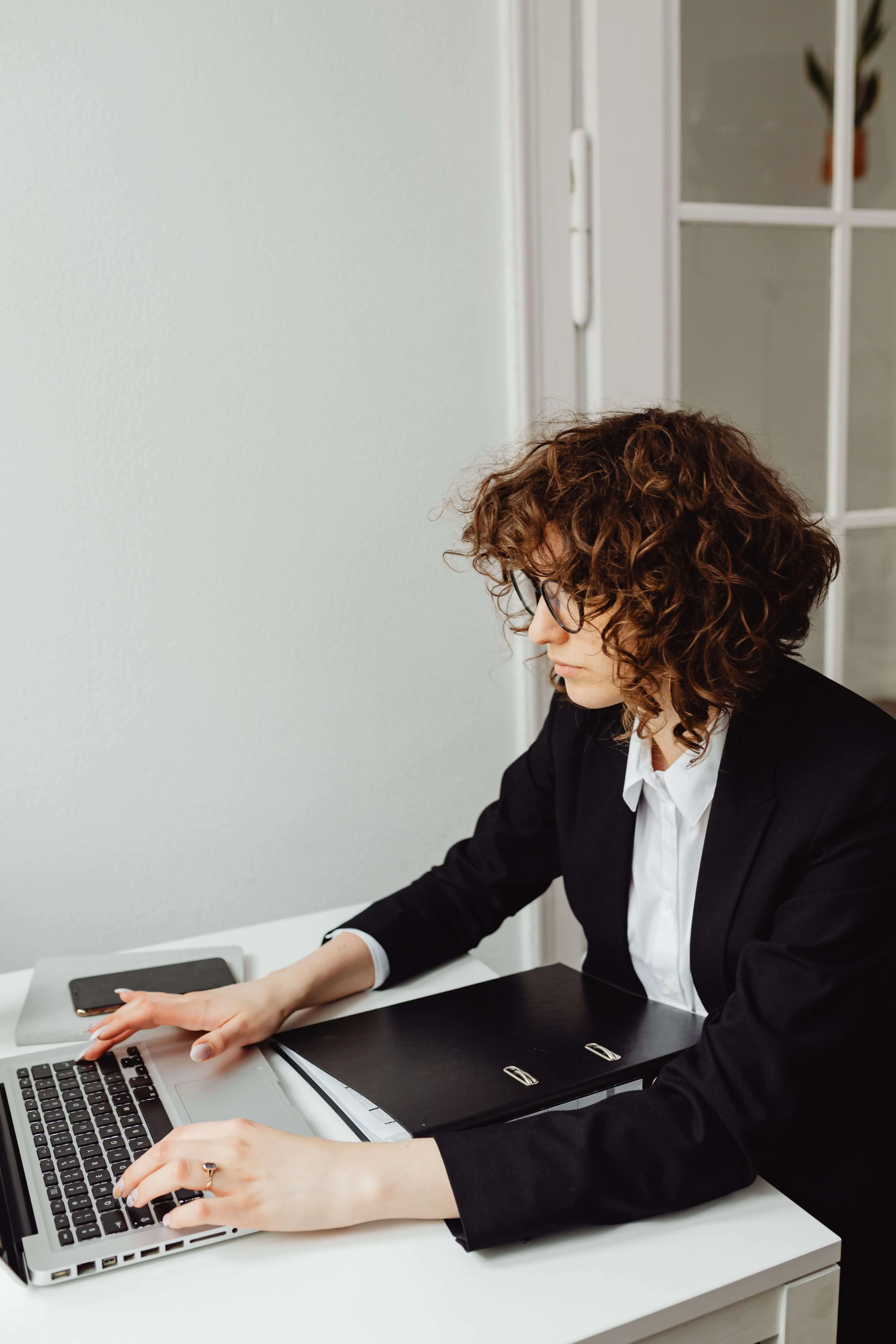 A woman in a dark suit reviewing a folder at her laptop