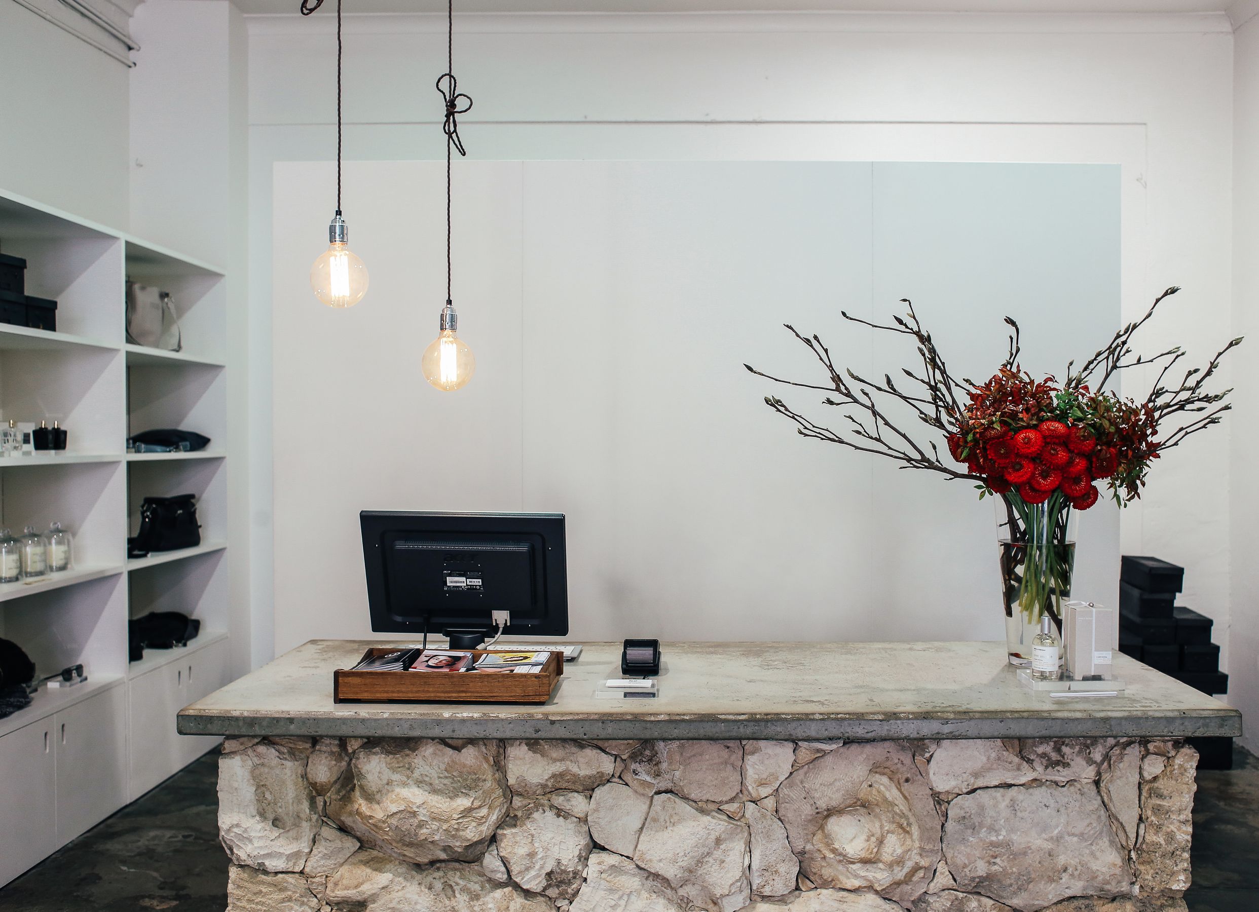 A stone reception desk with a computer, pendant lights and a vase of red flowers