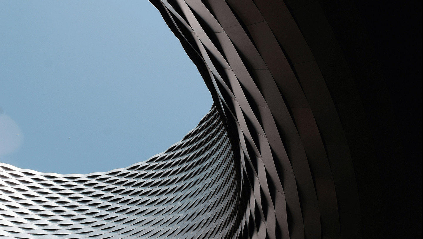 Curved modern architectural structure with diamond-shaped metal panels against a clear blue sky.