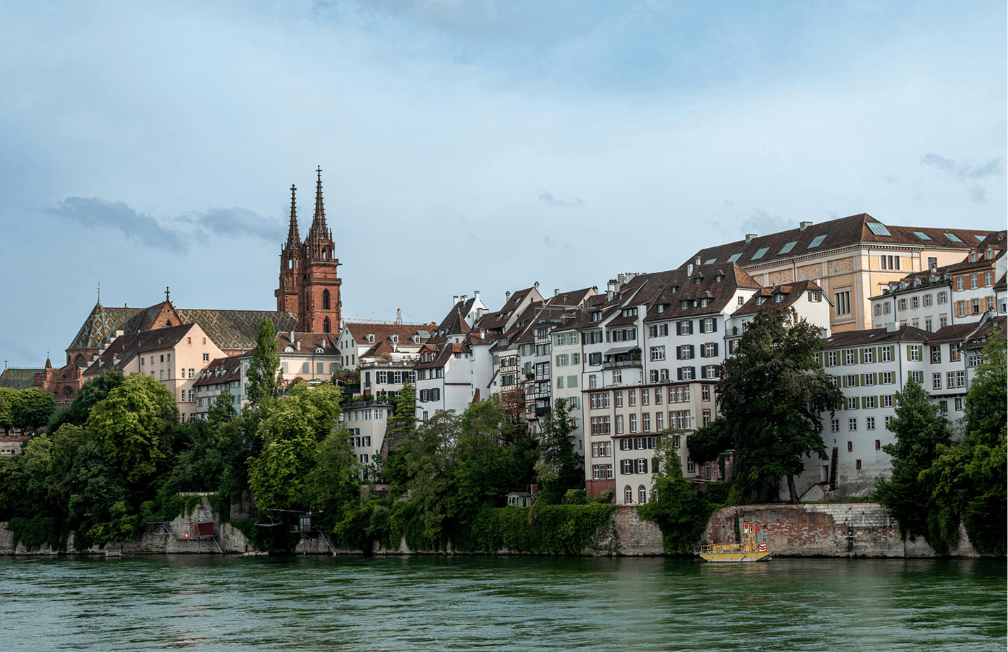 View of historic buildings and twin-spired Basel Minster cathedral along the Rhine River in Basel, Switzerland.