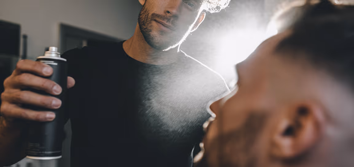 Man spraying another man's face with a black spray can indoors.