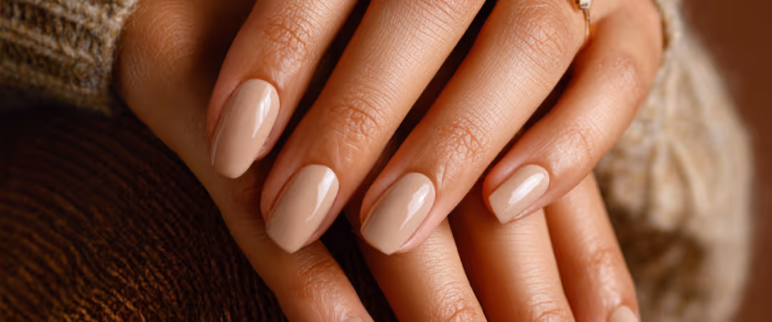 Close-up of hands with beige nail polish and a gold ring on a finger.