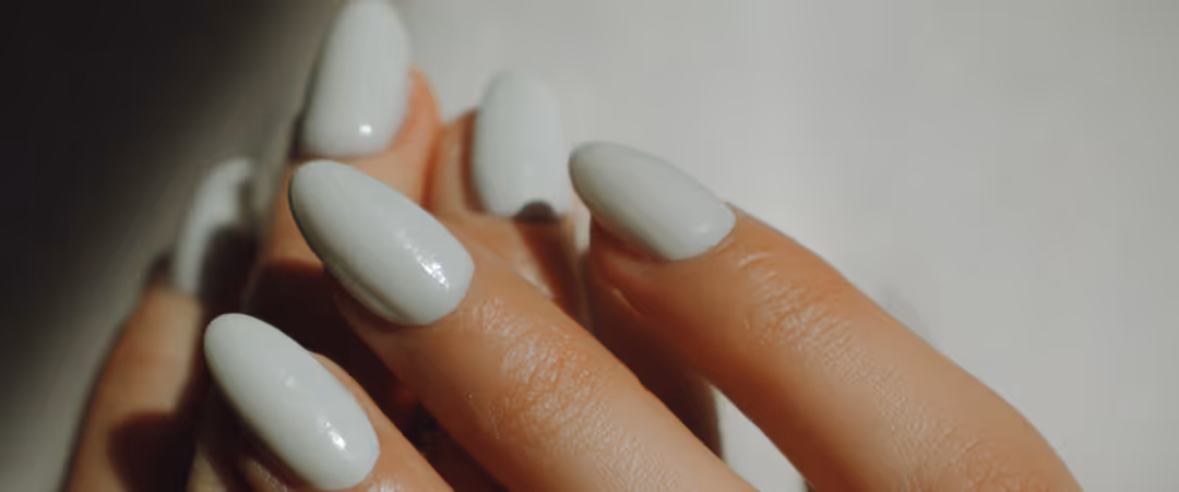 Close-up of a hand with glossy white almond-shaped nails against a light background.