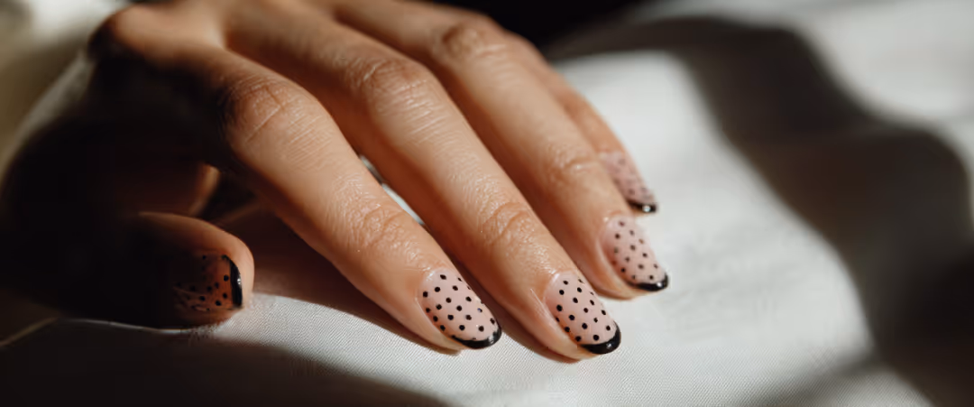 Hand with nails painted in light pink with black polka dots and black tips.