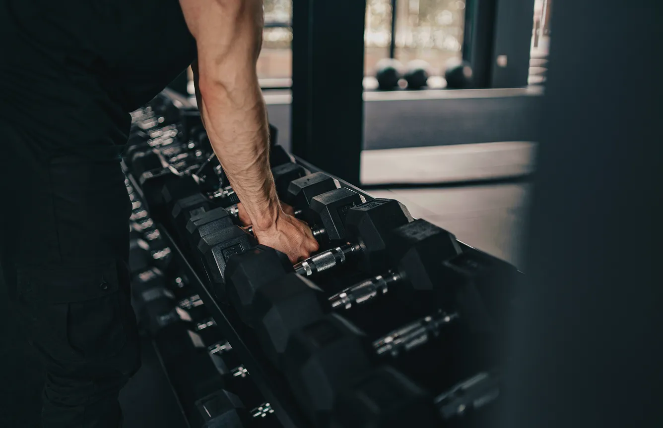 Person reaching for dumbbells on a rack in a modern gym.