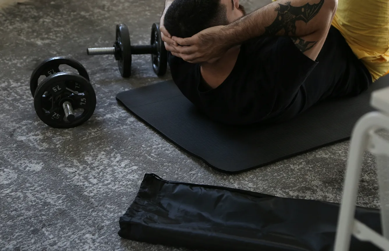Man doing crunches on a mat with dumbbells placed nearby.