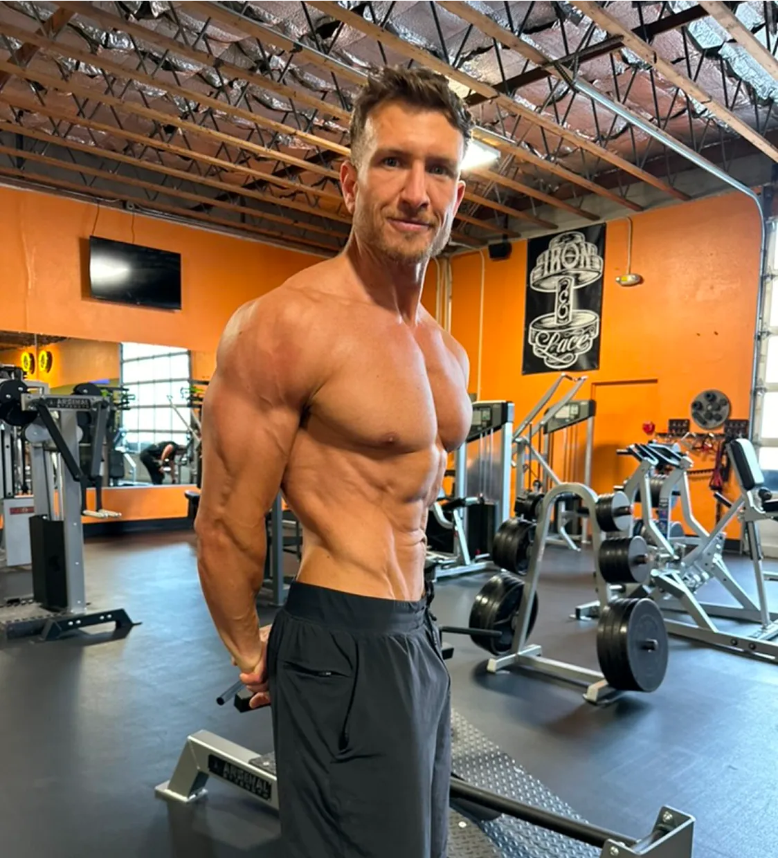 Shirtless man posing in a gym, showing muscular physique.