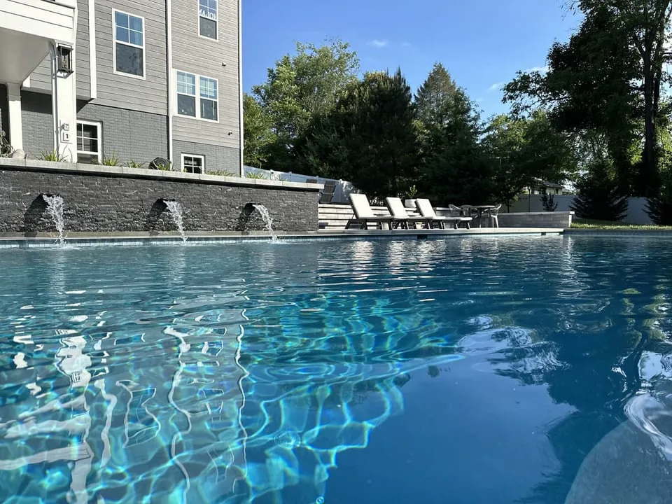 Gunite pool with waterfall feature and view of clear water by Deckscapes of Virginia