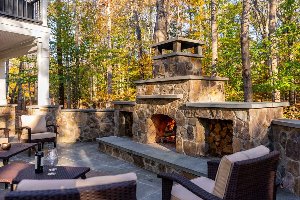 Large stone fireplace on patio with log storage by Deckscapes of VA