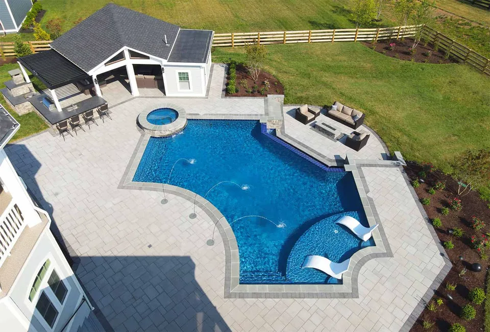 Modern backyard pool with fountains, lounge shelf, and pavilion with bar and firepit area by Deckscapes of Virginia