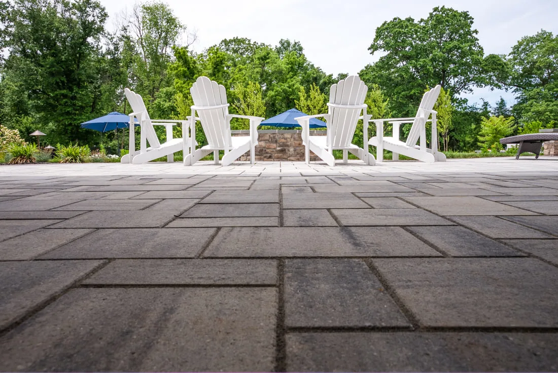 Paver patio detailing with four white Adirondack chairs surrounding custom fire pit