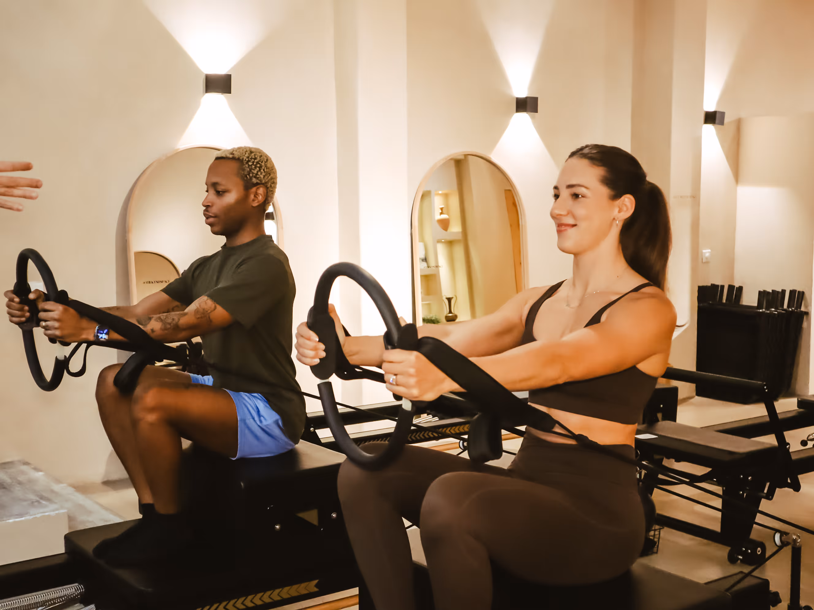 Two people doing Pilates with resistance rings on reformer machines in a bright studio.