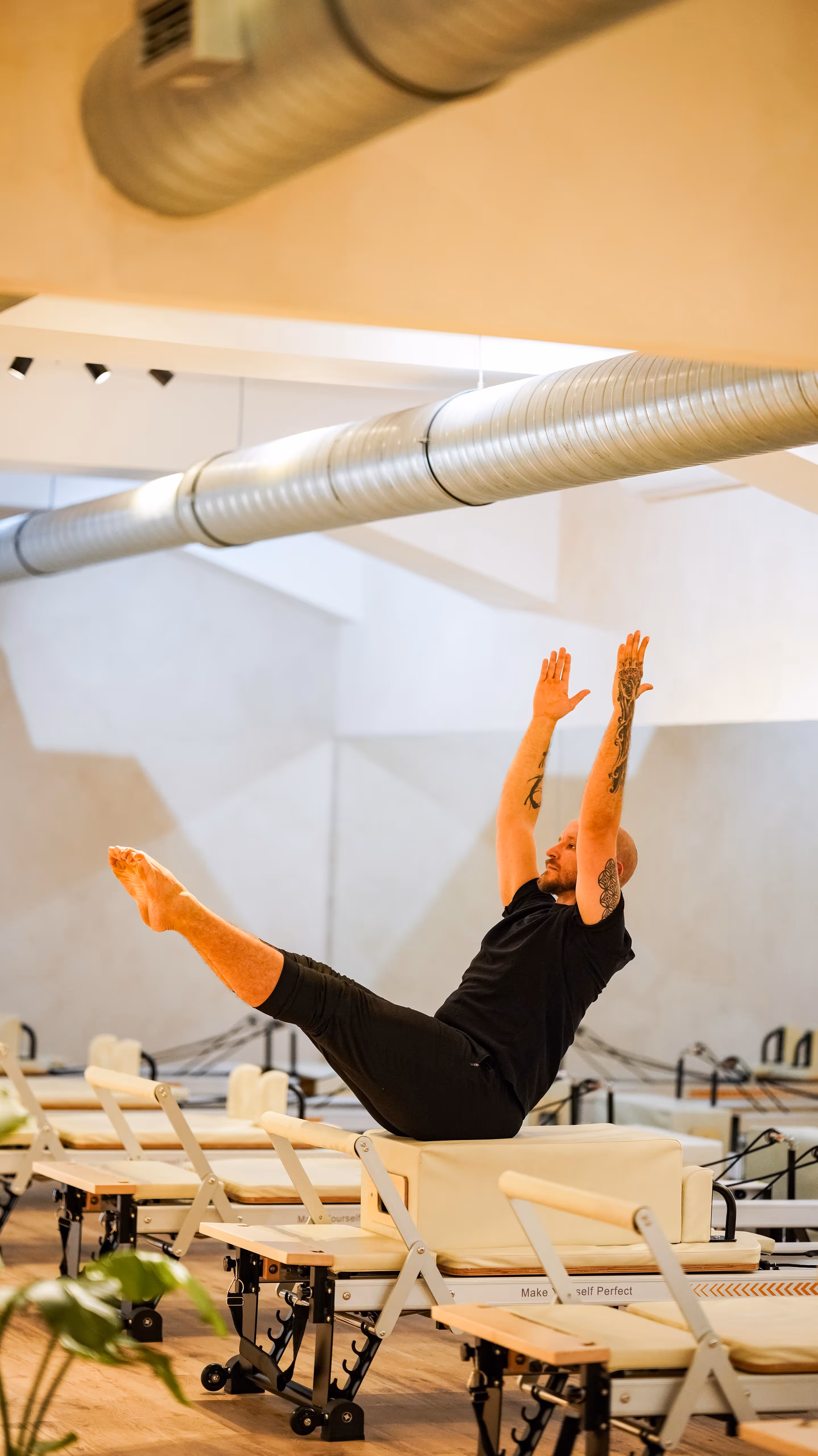 Man with tattoos doing a Pilates exercise on reformer machine in a bright studio.