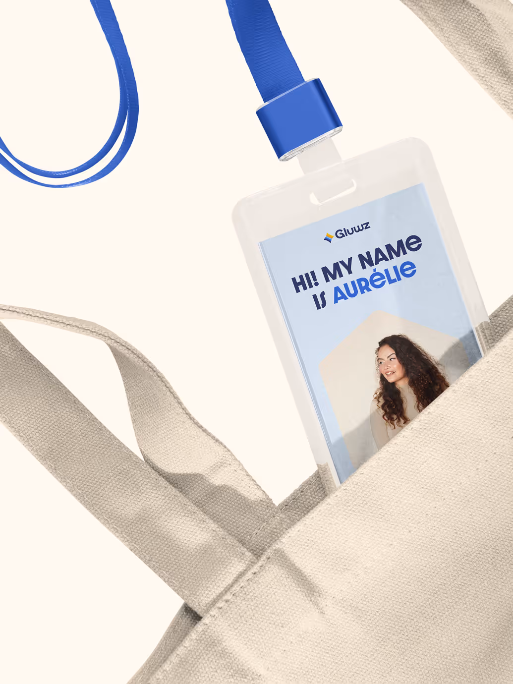 Name tag with blue lanyard and text 'Hi! My name is Aurélie' partially tucked into a beige fabric bag.