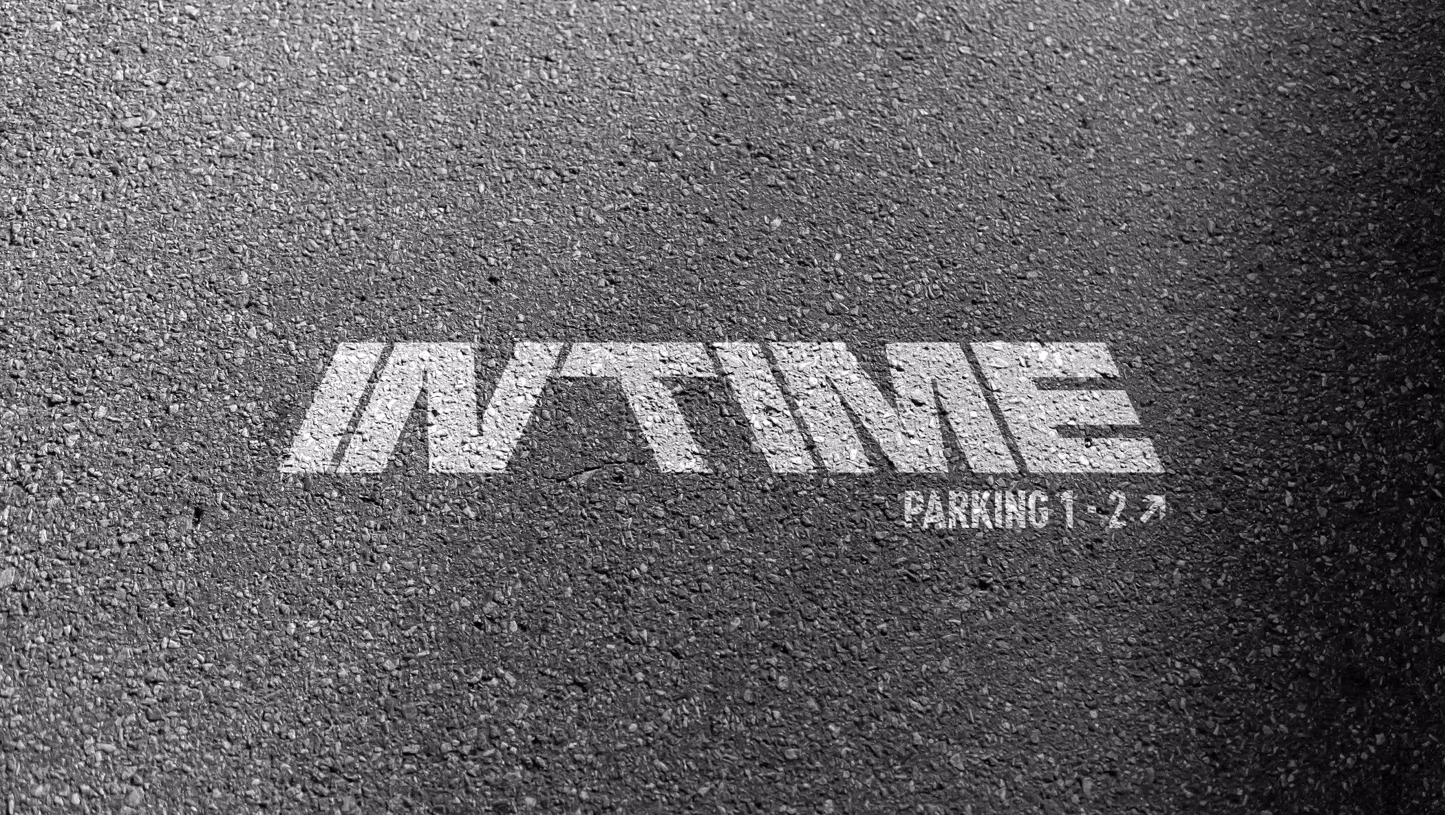 White painted text on asphalt reading 'IN TIME' with smaller text 'PARKING 1-2' and an arrow pointing right.