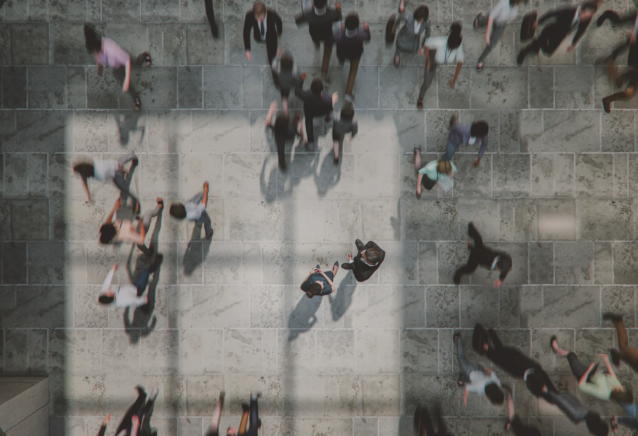 Top-down view of people walking on a stone-tiled sidewalk with shadows cast by a large window frame.