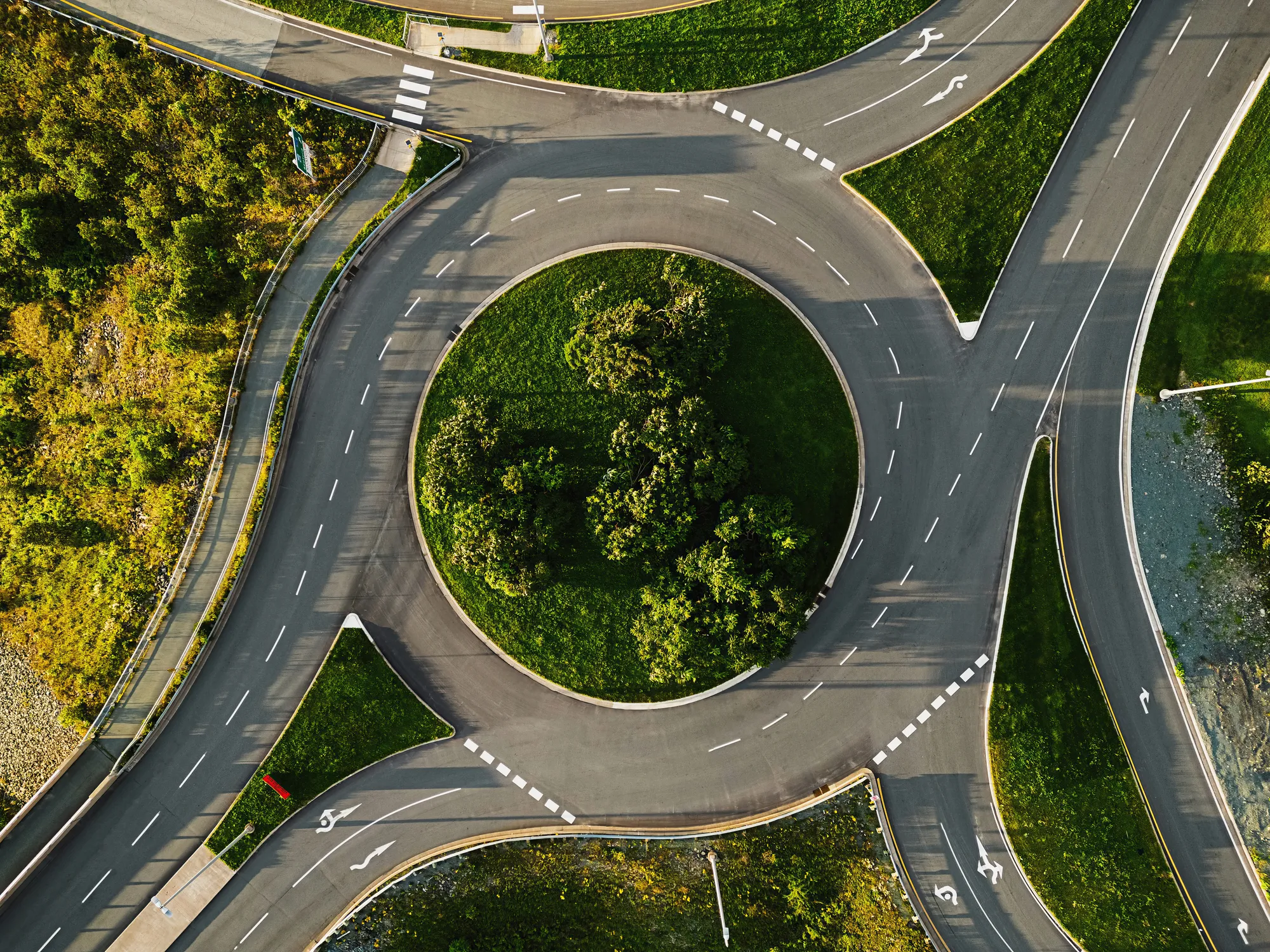 Aerial view of a roundabout with a green, tree-covered center surrounded by multiple lanes and roads.