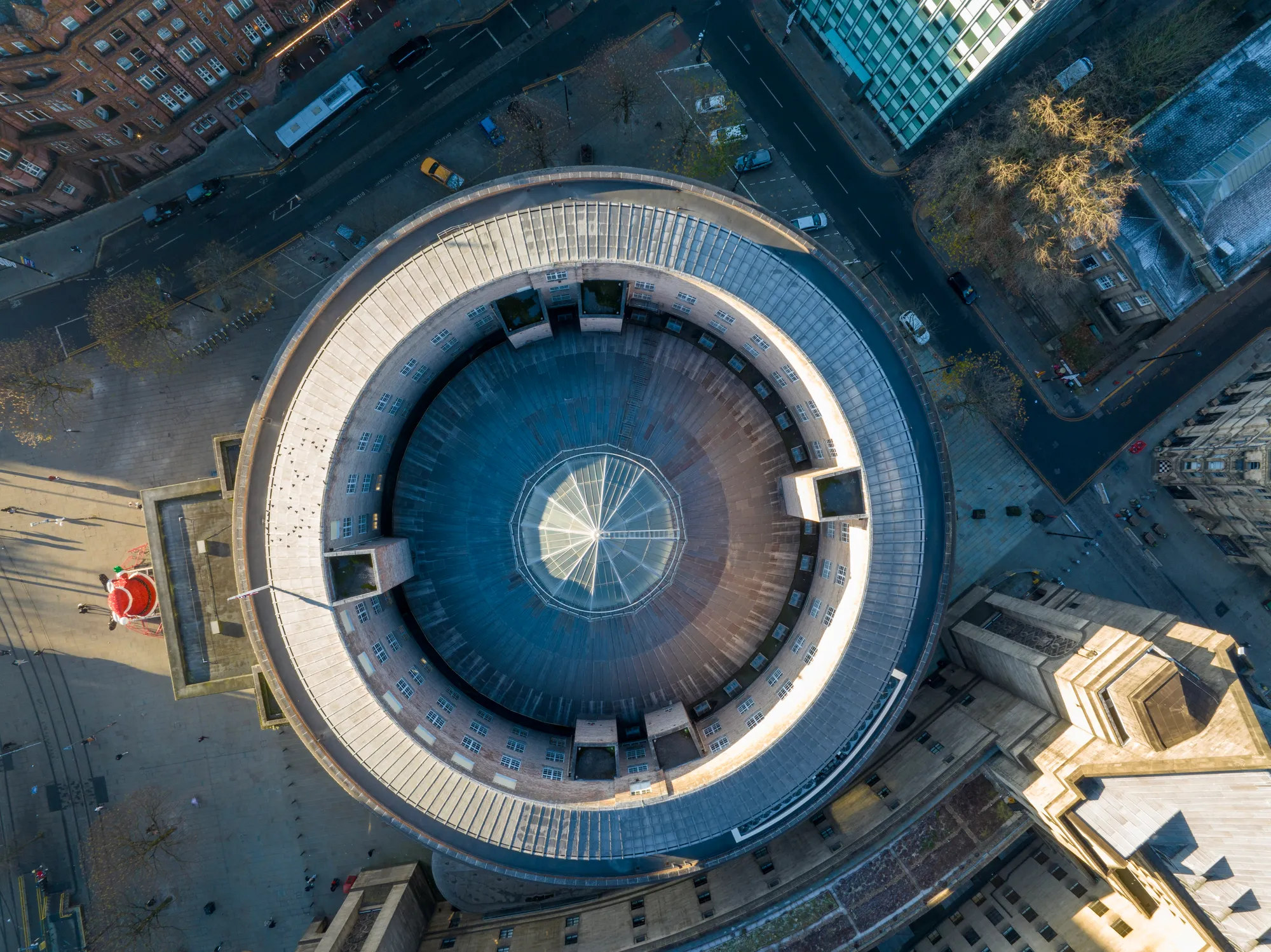 Aerial view of a circular building with a glass dome roof surrounded by city streets and adjacent buildings.