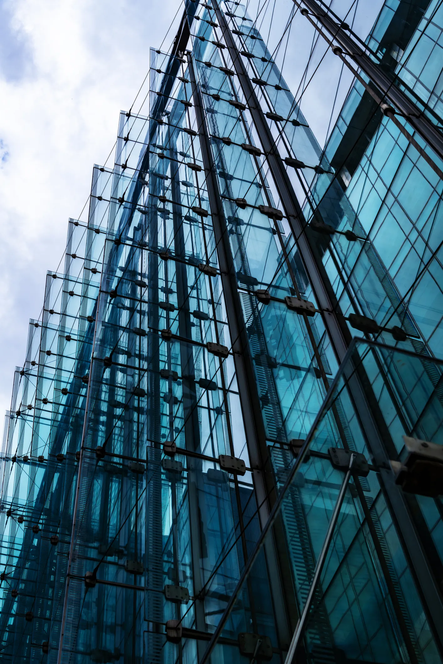 Upward view of a modern glass building facade with metal supports and reflections.