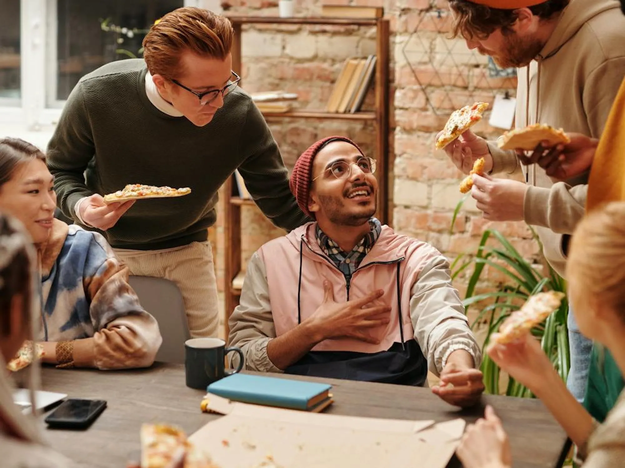 Group of young adults enjoying pizza together around a table in a casual, cozy indoor setting.
