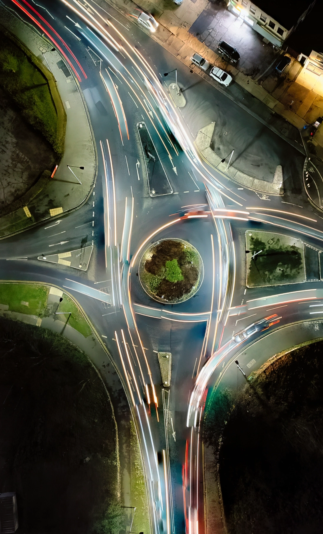 Aerial night view of a roundabout with car light trails showing vehicle movement on multiple lanes.